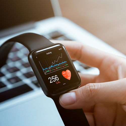 A hand holding a smartwatch over a laptop.