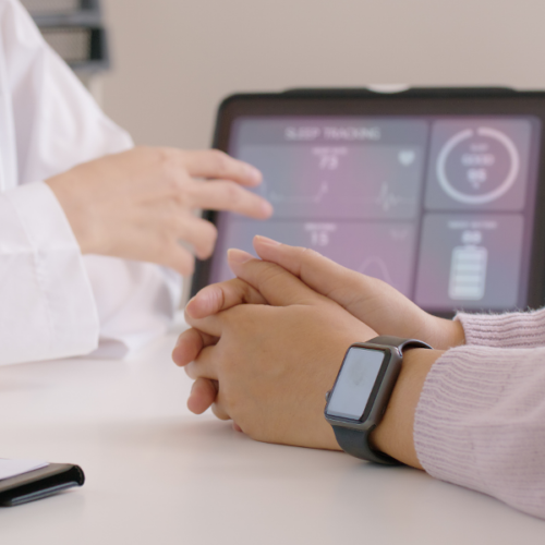 Close-up of a clinician gesturing to a tablet with health information and a patient wearing a smart watch.