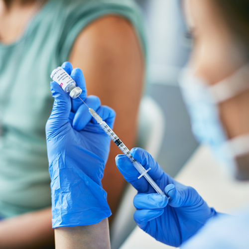 A masked clinician prepares a syringe of a vaccine.