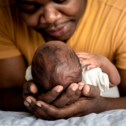 A person cradles their newborn's head in their hands.