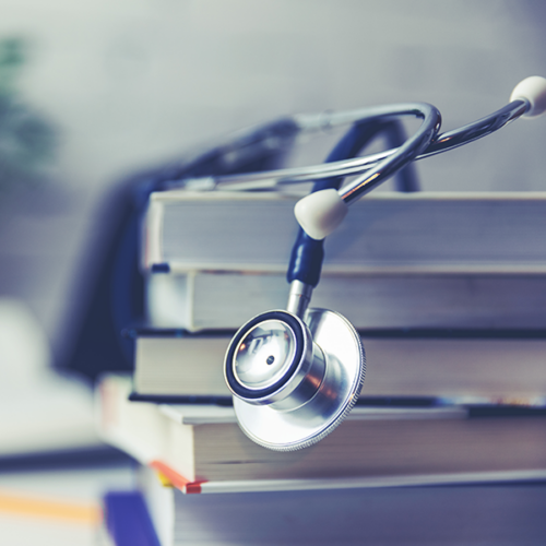 A stethoscope draped over a pile of books.