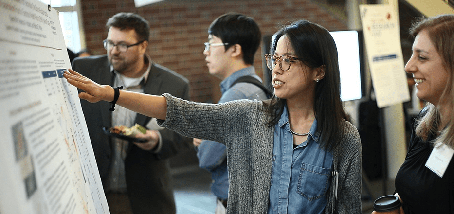 Sherry Xie points at a research poster.